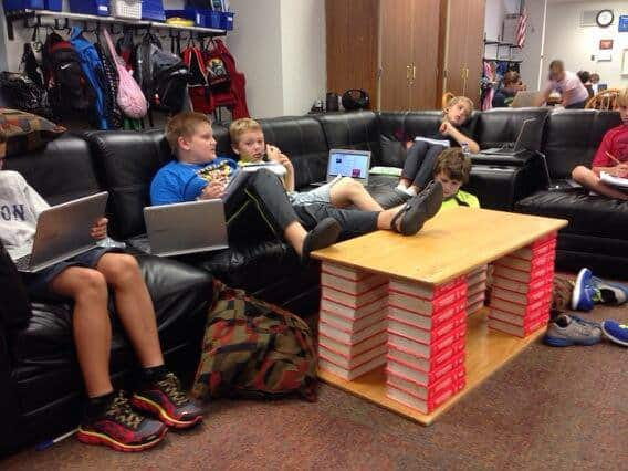 Students sit around a creatively built table with laptops. 