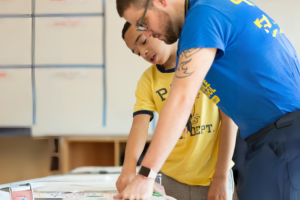 A teacher at Capital City Public Charter School provides feedback on a student’s science poster. (Expanded with AI).